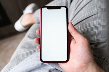 Young man hands holding mobile smart phone with mockup white blank display, empty screen at home. Shopping, delivery apps, social media applications ads,  close up view.