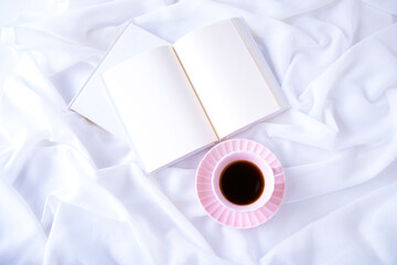 白い布の上のピンクのコーヒーカップと見開きの本
