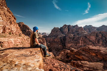 tourist sitting on the rock at the red rocky mountains in jordan - obrazy, fototapety, plakaty