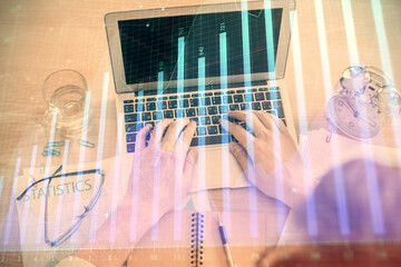 Double exposure of man's hands typing over laptop keyboard and forex chart hologram drawing. Top...