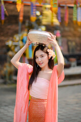 cheerful smiling asian woman splashing water in traditional lanna style dress in thai temple , Songkran festival concept