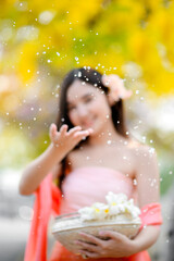 blur of asian woman splashing water in traditional lanna style dress with blooming golden shower flower, Songkran festival concept