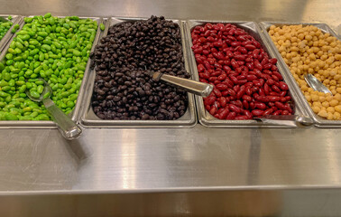 Different types of beans on buffet trays on salad bar.