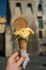 Woman's hand holds a delicious dessert in a waffle glass against the backdrop of sunny Italy.