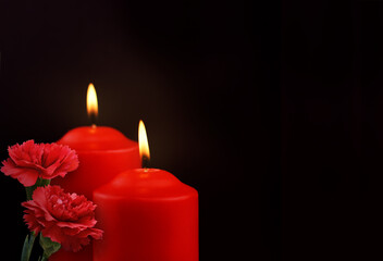 Two red burning candles and of carnation flowers on black background