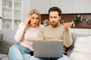 Young caucasian couple having financial problems. Frustrated wife and upset husband looking through bills on the laptop. Young spouses unable to pay for the mortgage