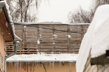 A wooden crate of a dismantled roof with hanging icicles on the edge. An old house against the backdrop of a gray sky. Large cascades, even beautiful rows. Cloudy winter day, soft light. UHD 4K.