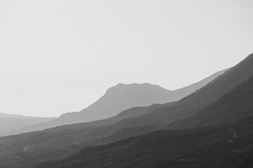 Grayscale shot of sand and mountains in the desert with foggy weather