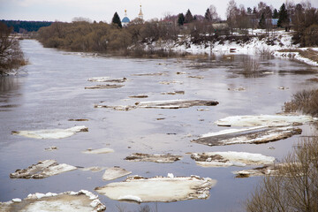 A group of large white ice floes are floating down the river. Spring, snow melts, dry grass all around, floods begin and the river overflows. Day, cloudy weather, soft warm light.