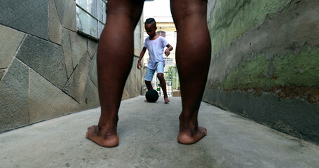 African father and child boy playing soccer together at home alley