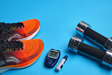 Orange sneakers, metal dumbbells and a blood glucose meter on a blue background - obrazy, fototapety, plakaty