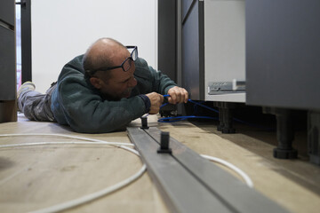 Mature technician installing plastic tubes to connect water filter to an american refrigerator in...