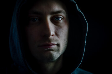 Portrait of a young man with a hood on his head looking grumpy in a dark atmosphere