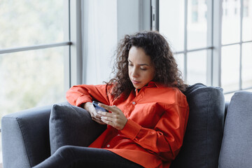 young woman uses smartphone to type messages on the sofa at home.