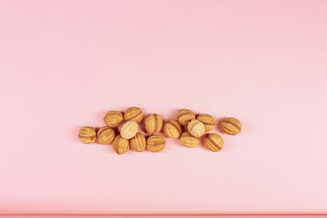delicious walnut shaped shortbread sandwich cookies filled with sweet condensed milk and chopped pistachio nuts on brown clay dish. on pink background, view from above, close-up