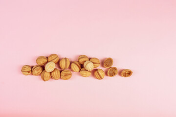 delicious walnut shaped shortbread sandwich cookies filled with sweet condensed milk and chopped pistachio nuts on brown clay dish. on pink background, view from above, close-up