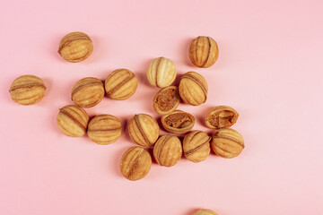 delicious walnut shaped shortbread sandwich cookies filled with sweet condensed milk and chopped pistachio nuts on brown clay dish. on pink background, view from above, close-up