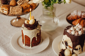 Traditional Ukrainian Easter cake decorated with a nest with eggs and a candle. Traditional dessert. Easter cake stands on a festive table decorated with sweets.