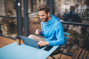 Smiling male freelancer browsing funny video content while networking in social media using netbook...