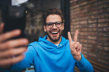 Happy millennial user smiling at cellular camera while shooting video content for sharing to social...