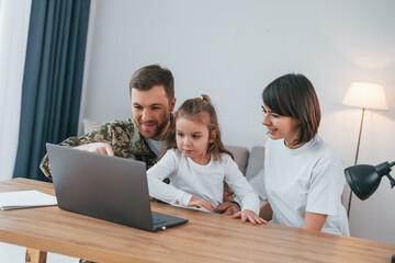 Obraz premium Talking by using laptop. Soldier in uniform is at home with his wife and daughter