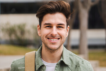 Caucasian happy male in university campus. Portrait of teenage male student standing in a college - obrazy, fototapety, plakaty