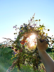 floral wreath in hand, sunny natural background.  floral traditional decor for Summer Solstice Day, Midsummer concept. pagan witch traditions, wiccan symbol and rituals