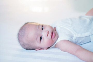 Asian baby in white is sleeping on the bed.