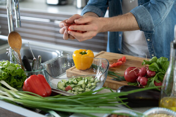 Young man preparing vegetable salad in the kitchen. Happy man making healthy meal