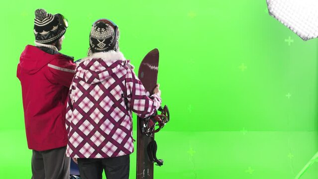  young couple with snowboard and enjoys the view. Guy and girl in warm clothes on a green background in the studio. Chroma key 