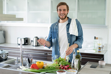 Young man preparing vegetable salad in the kitchen. Happy man making healthy meal