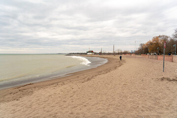 A lone figure walks on Toronto's Kew Beach on a spring evening with the city skyline in the far back ground.  Room for text.
