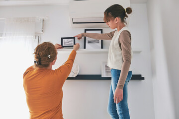 Mother and daughter hanging pictures and photos at home.