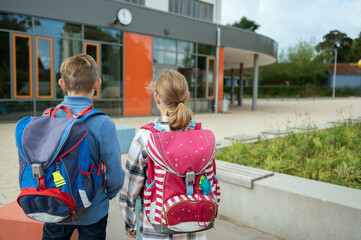 Two teen students with backpacks waiting in front of modern school