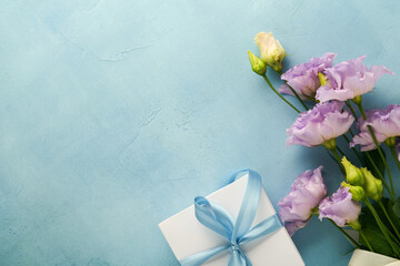 Festive flower composition purple color and gift box with ribbon on light blue concrete background. Mothers day concept. Flowers frame. Overhead view. Top view with copy space.