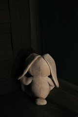 Abandoned bunny coveres his eyes, sitting in the corner. Child abuse concept. Vertical image