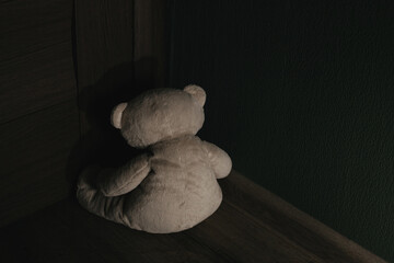 Teddy bear is sitting in the corner of the dark room. Child abuse and punishment concept