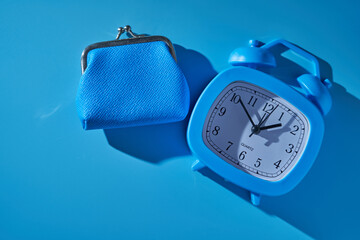 alarm clock and blue coin purse against blue background