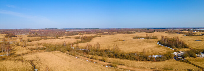 Aerial view of fields with copse, dry yellow grass, a stream, remnants of snow in early spring. Nature background.