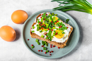 Sandwich with curd cheese, boiled egg and green onions, sprinkled with pink pepper on a light background. Simple and healthy breakfast