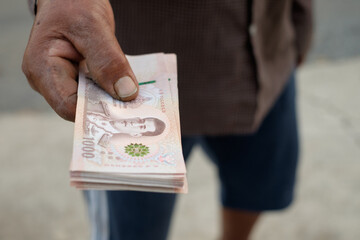 One thousand baht banknotes held in the hands of an elderly farmer.