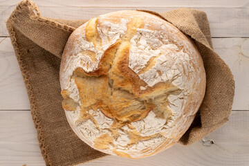 One loaf of fresh fragrant white wheat bread with a jute bag on a wooden table, macro, top view.