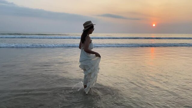 Slow motion woman wearing a white dress walking enjoy on the beach with beautiful sunset on summer vacation in Phuket, Thailand
