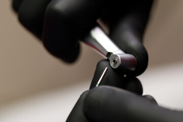 Close-up shot of a dental drill without a tip. A dentist or dental technician in black gloves is...