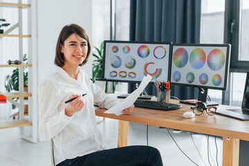 With paper. Female designer working in the office by using PC
