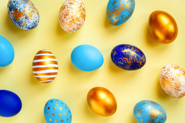 colored Easter eggs of different colors, blue, gold and multi-colored and spotted on a yellow background for the traditional religious holiday of holy easter