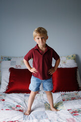 young boy stands on a bed posing for a picture
