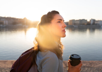 sunset photo of a pretty young woman holding a cup of coffee