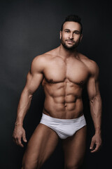 Fototapeta na wymiar Handsome man in white underwear standing in studio at dark grey background