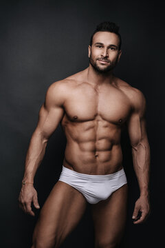 Handsome man in white underwear standing in studio at dark grey background
